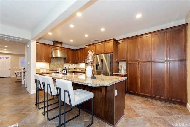 kitchen featuring exhaust hood, a sink, a kitchen bar, visible vents, and stainless steel fridge with ice dispenser