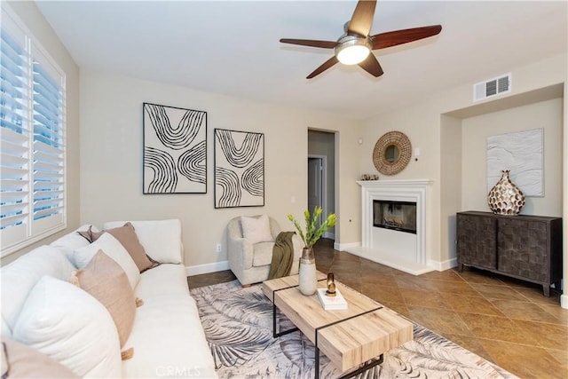 living room featuring a glass covered fireplace, visible vents, ceiling fan, and baseboards