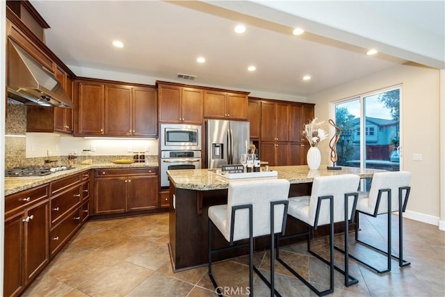 kitchen featuring light stone countertops, a breakfast bar, appliances with stainless steel finishes, a kitchen island, and visible vents