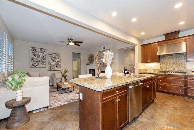 kitchen featuring light stone countertops, appliances with stainless steel finishes, a sink, a ceiling fan, and wall chimney exhaust hood