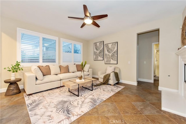 living area featuring baseboards, a ceiling fan, and a glass covered fireplace