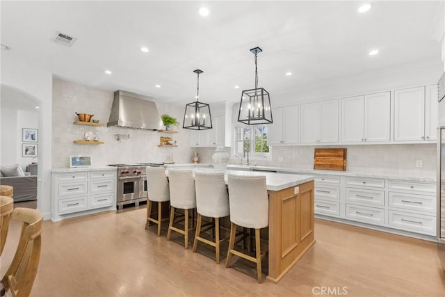 kitchen with recessed lighting, wall chimney exhaust hood, light wood finished floors, and range with two ovens