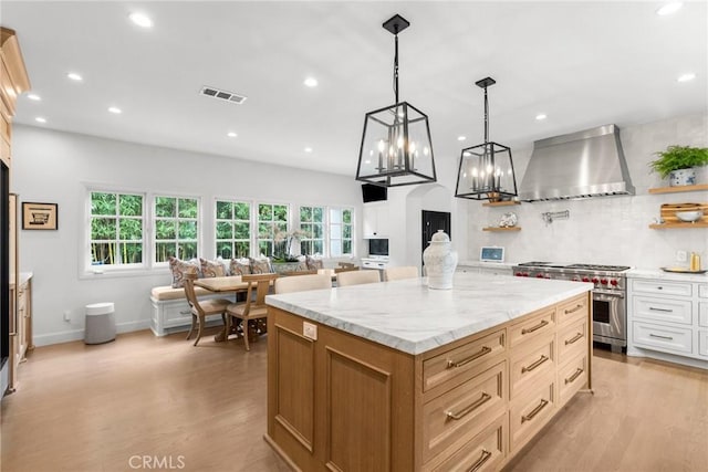 kitchen featuring light wood finished floors, plenty of natural light, stainless steel stove, and wall chimney range hood