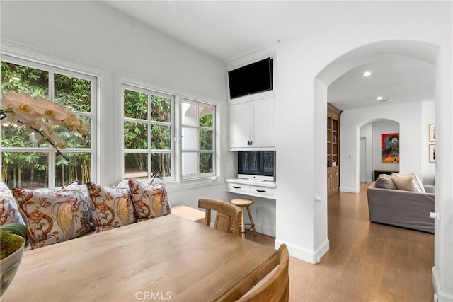 dining space featuring arched walkways, light wood-style floors, a wealth of natural light, and baseboards