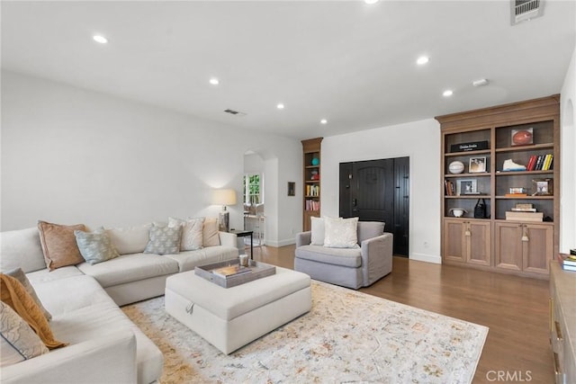 living room with arched walkways, light wood-style flooring, visible vents, and recessed lighting