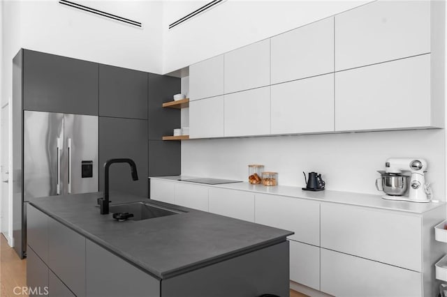 kitchen with a sink, open shelves, high end fridge, an island with sink, and modern cabinets