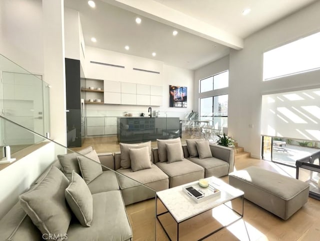 living room with light wood-type flooring, a towering ceiling, recessed lighting, and beam ceiling