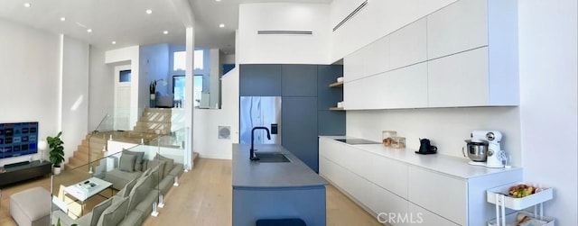 kitchen featuring light wood finished floors, a sink, open shelves, white cabinets, and modern cabinets