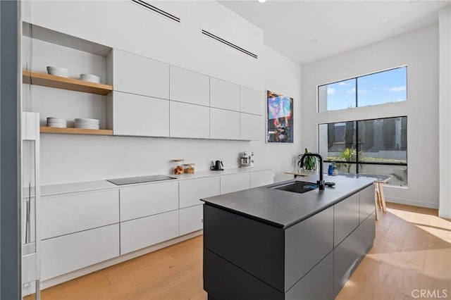 kitchen featuring light wood finished floors, modern cabinets, a sink, a center island with sink, and white cabinets