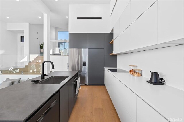kitchen with modern cabinets, light wood finished floors, a sink, stainless steel appliances, and white cabinets