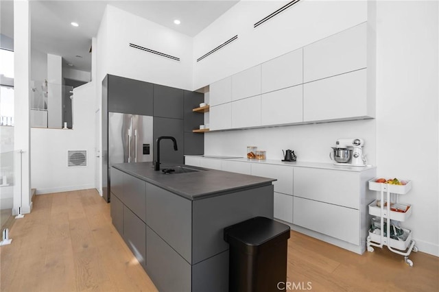 kitchen featuring a sink, a center island with sink, light wood-style flooring, white cabinets, and modern cabinets