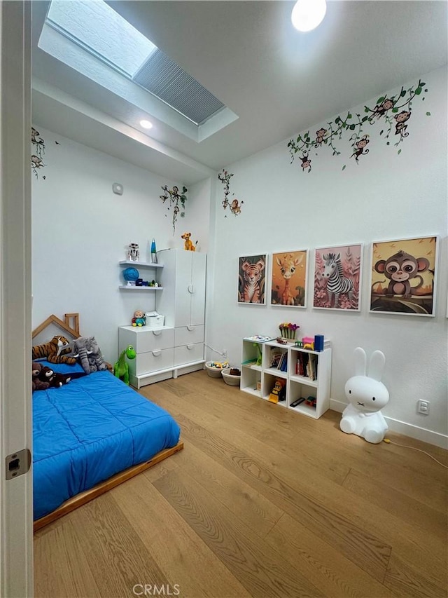bedroom featuring baseboards, a skylight, and wood finished floors