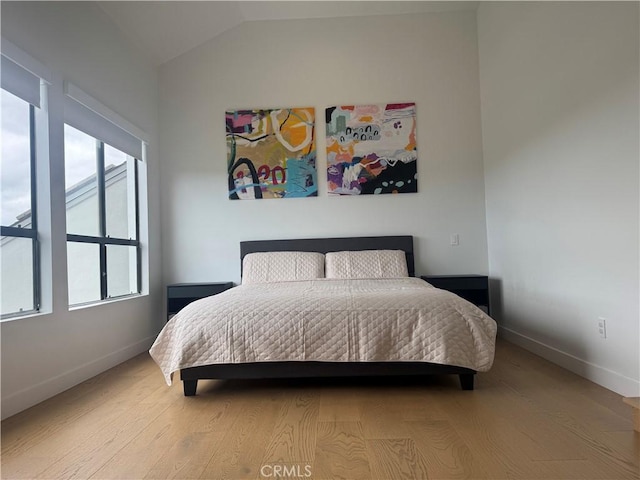 bedroom with vaulted ceiling, baseboards, and wood finished floors