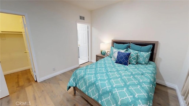 bedroom with wood finished floors, visible vents, a walk in closet, and baseboards