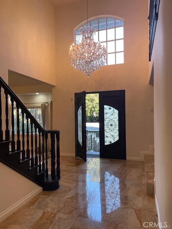 entryway featuring stairs, a chandelier, marble finish floor, baseboards, and a towering ceiling