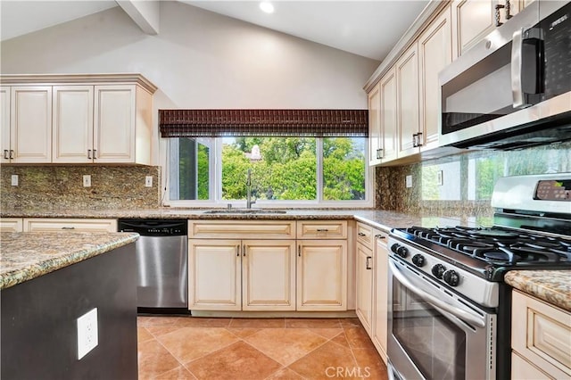 kitchen with vaulted ceiling, tasteful backsplash, a sink, cream cabinetry, and appliances with stainless steel finishes