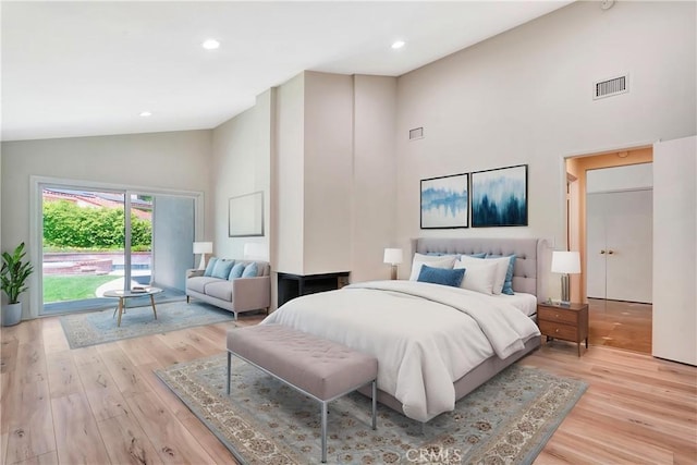 bedroom featuring high vaulted ceiling, light wood-style floors, visible vents, and access to exterior