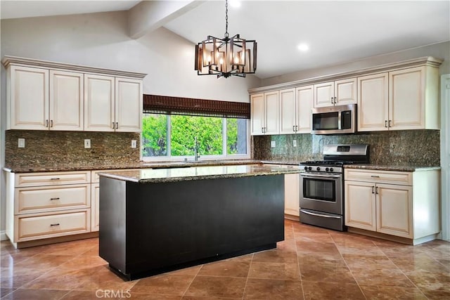 kitchen with a sink, dark stone counters, cream cabinets, appliances with stainless steel finishes, and a notable chandelier