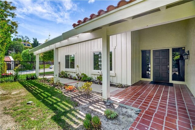 entrance to property with board and batten siding, a patio area, and fence