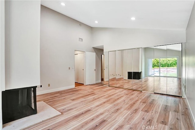 unfurnished living room with high vaulted ceiling, light wood-style floors, and a multi sided fireplace