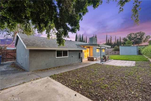 back of house at dusk featuring a chimney, a patio, stucco siding, and fence