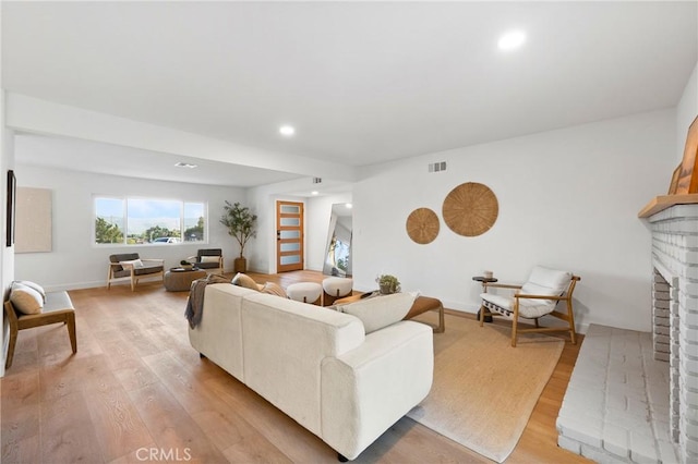 living room featuring light wood finished floors, baseboards, a brick fireplace, visible vents, and recessed lighting