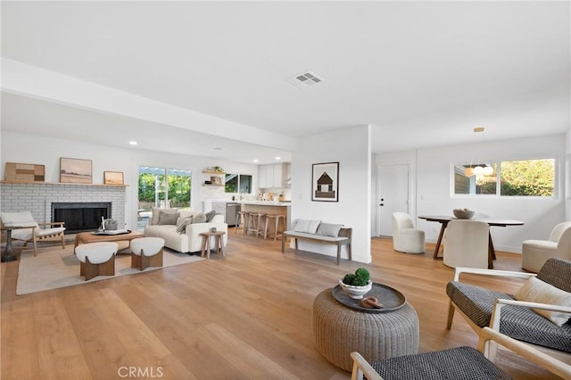 living area with recessed lighting, a brick fireplace, visible vents, and light wood-style flooring