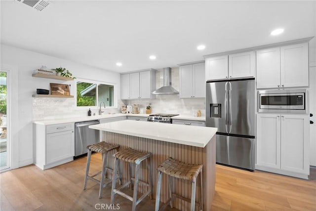 kitchen with wall chimney range hood, a sink, a breakfast bar, stainless steel appliances, and backsplash