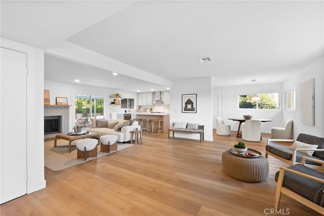 living area with light wood-type flooring, a brick fireplace, and plenty of natural light