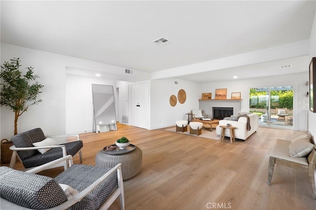 living room featuring light wood-style flooring, visible vents, and a brick fireplace