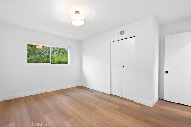 unfurnished bedroom featuring light wood finished floors, baseboards, visible vents, and a closet