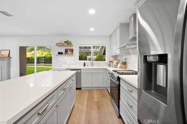 kitchen featuring backsplash, visible vents, a sink, wall chimney exhaust hood, and appliances with stainless steel finishes