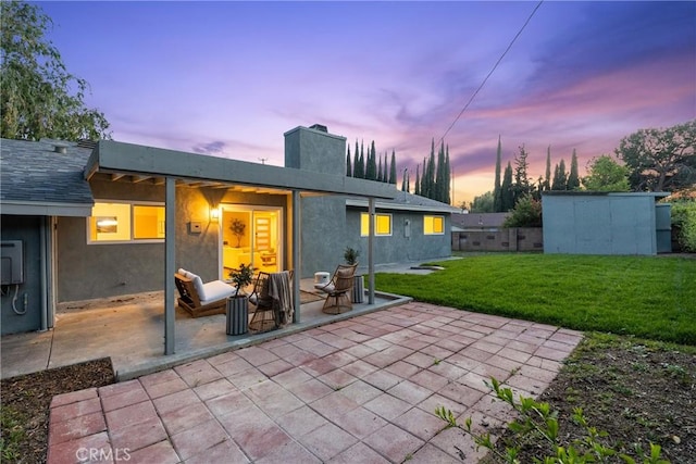 back of property featuring stucco siding, a lawn, a chimney, and a patio