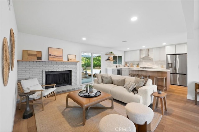 living area with light wood-style flooring, a brick fireplace, and recessed lighting