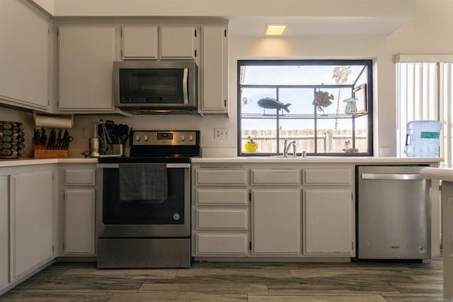kitchen featuring wood finished floors, light countertops, white cabinets, a sink, and appliances with stainless steel finishes