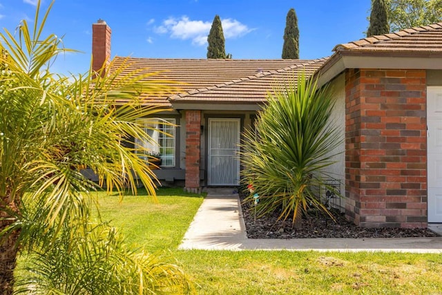 entrance to property with a lawn, a tile roof, and brick siding