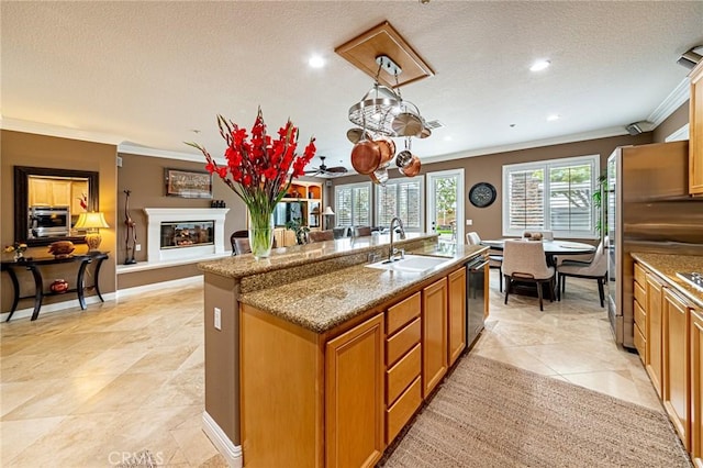 kitchen with appliances with stainless steel finishes, a sink, a textured ceiling, a center island with sink, and ornamental molding