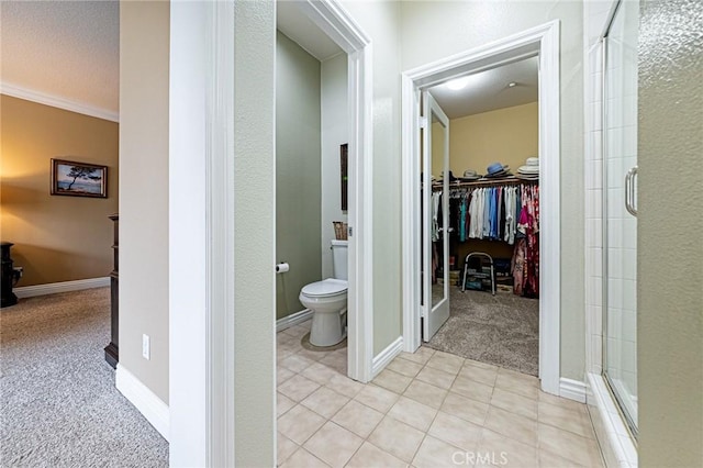 bathroom featuring crown molding, toilet, baseboards, a shower stall, and a spacious closet