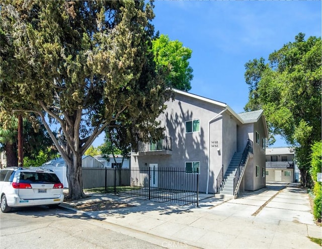 view of front of home featuring stucco siding, stairway, driveway, and fence private yard