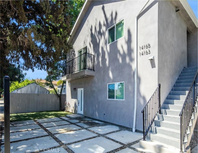 exterior space featuring stairway, fence, a balcony, stucco siding, and a patio