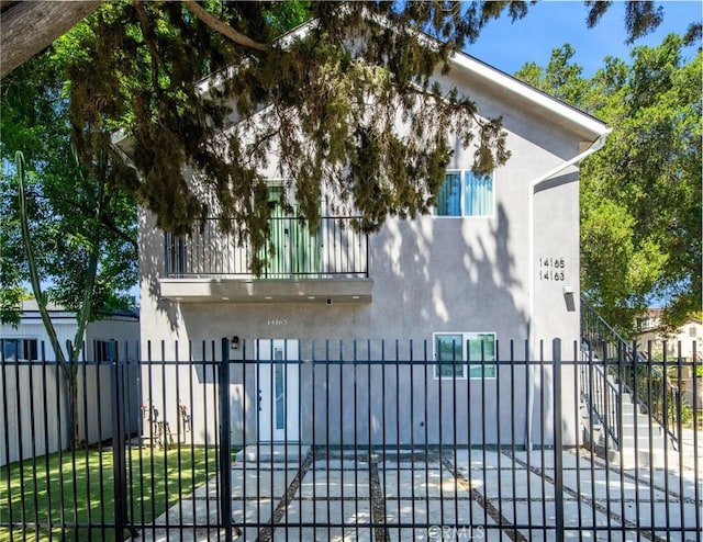 view of side of property featuring stucco siding, a balcony, and a fenced front yard