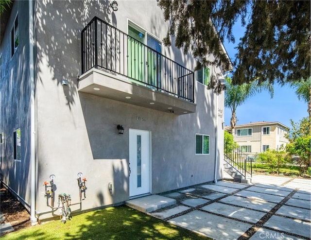 rear view of house with stucco siding, a patio, and a balcony
