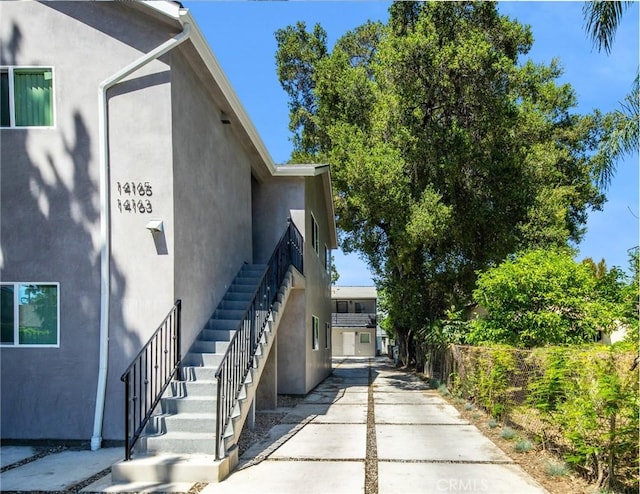 view of side of home featuring stairway, concrete driveway, fence, and stucco siding