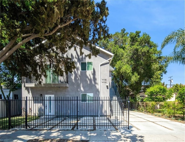 view of side of home featuring concrete driveway, stucco siding, a balcony, and a fenced front yard