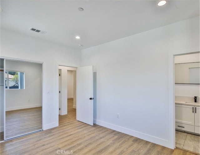 unfurnished bedroom featuring light wood finished floors, a sink, baseboards, visible vents, and recessed lighting
