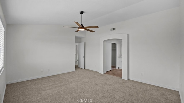 carpeted spare room with visible vents, arched walkways, baseboards, and a ceiling fan