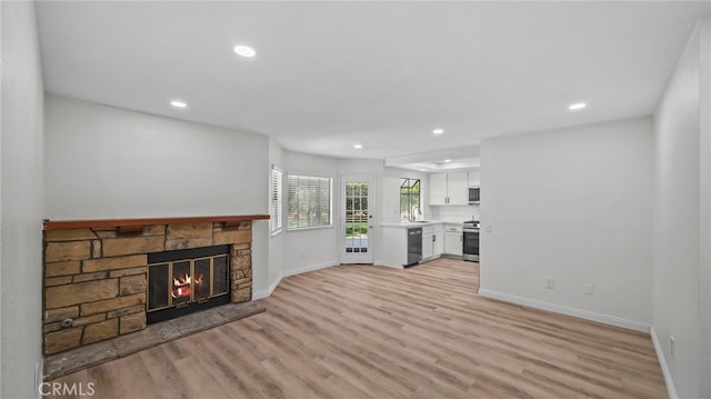 unfurnished living room featuring light wood-style floors, a sink, baseboards, and a stone fireplace