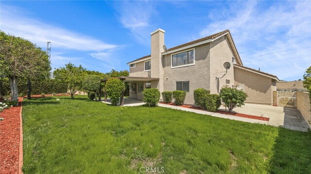 back of house with a chimney, fence, a yard, a patio, and stucco siding