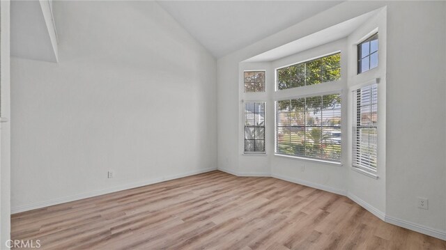 unfurnished room with high vaulted ceiling, plenty of natural light, baseboards, and light wood-style floors