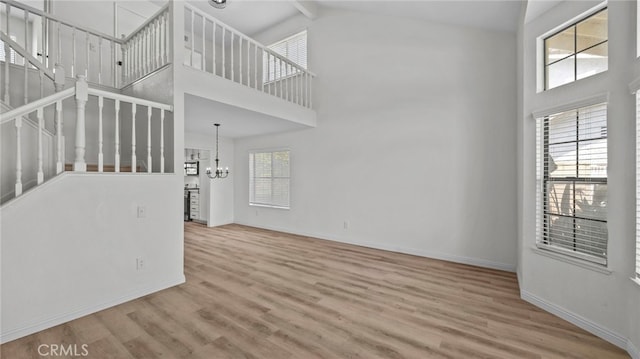 unfurnished living room featuring baseboards, high vaulted ceiling, a chandelier, and wood finished floors